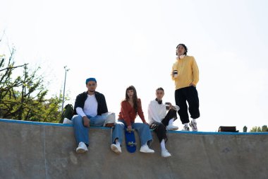 Dört genç arkadaş kaykay parkında rahatlar, gülüşürler ve güneşin altında içkilerini yudumlarlar..