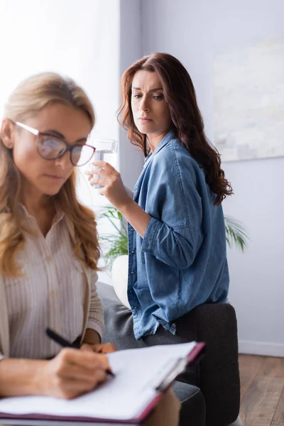 Therapist writing in medical history while patient drinking water — Stock Photo