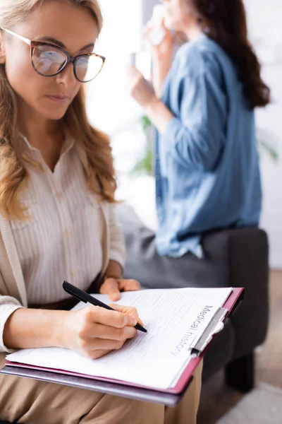 Terapeuta escribiendo en la historia clínica del paciente - foto de stock