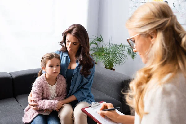 Madre preocupada abrazando a su hija mientras visita al psicólogo - foto de stock