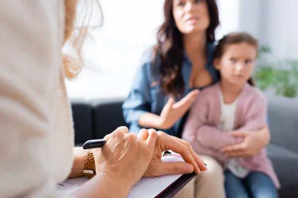 Blurred view of worried mother showing at daughter while visiting psychologist — Stock Photo