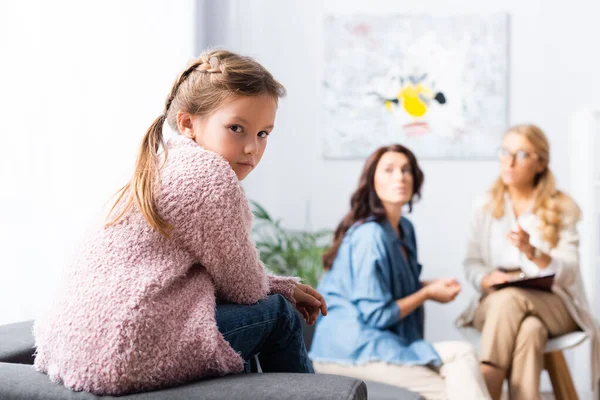 Hija sentada en el sofá mientras la madre habla con el psicólogo - foto de stock