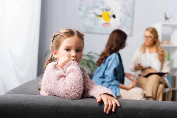 Hija sentada en el sofá mientras la madre habla con el psicólogo - foto de stock