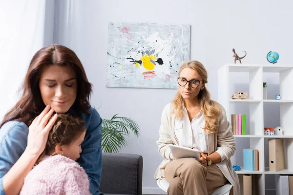 Worried mother with closed eyes hugging daughter while visiting psychologist — Stock Photo