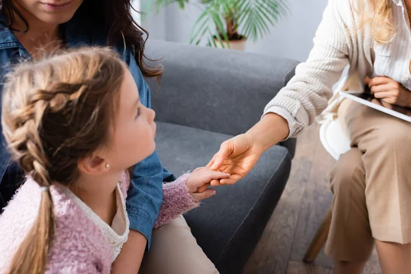 Niña pequeña paciente sentada con la madre y dando la mano al psicólogo - foto de stock