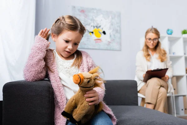 Infeliz niña con juguete visitando psicólogo - foto de stock