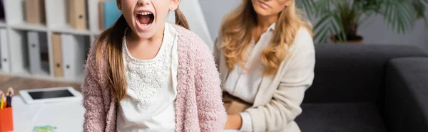 Обрізаний вид сердитої дівчинки кричить під час відвідування психолога, банер — стокове фото