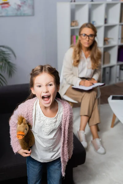 Menina zangada com brinquedo gritando enquanto visita psicólogo — Fotografia de Stock