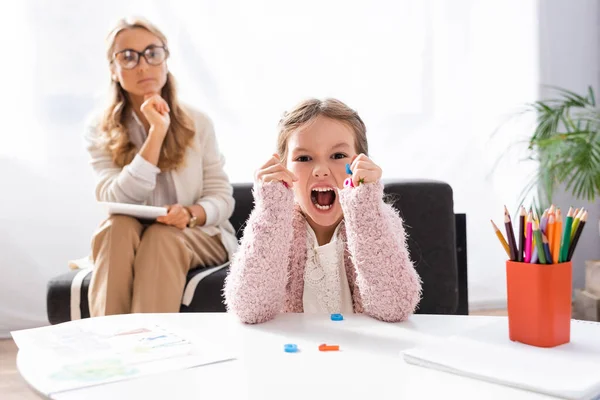 Маленькая девочка пациентка кричит и сжимает фигуры во время посещения психолога — стоковое фото
