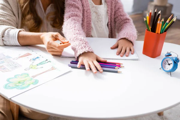 Recortado vista de niña dibujando imágenes con lápices de colores mientras visita psicólogo - foto de stock