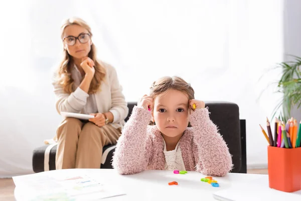 Маленька дівчинка дивиться на камеру і тримає барвисті фігури під час відвідування психолога — стокове фото