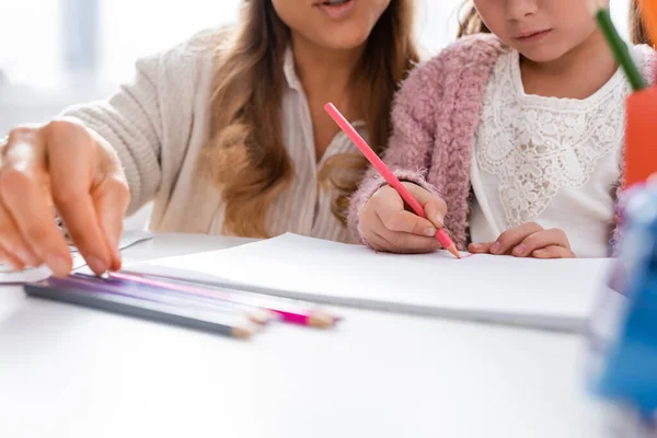 Recortado vista de niña dibujando imágenes con lápices de colores mientras visita psicólogo - foto de stock