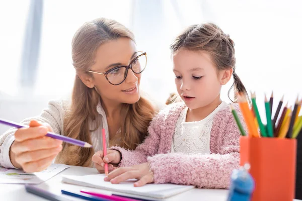 Niña haciendo dibujos con lápices de colores mientras visita a psicólogo - foto de stock