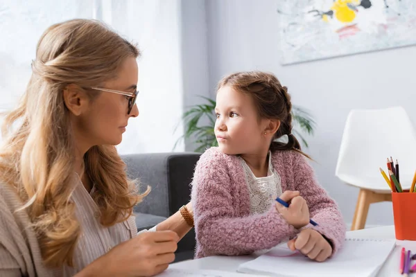 Kleines Mädchen schaut Psychologin an und hält Bleistift — Stockfoto