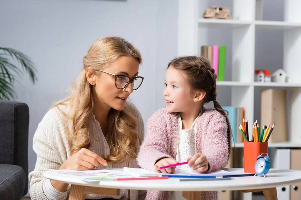 Little girl drawing pictures with colorful pencils while visiting psychologist — Stock Photo