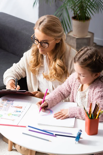 Little girl drawing pictures with colorful pencils while visiting psychologist — Stock Photo