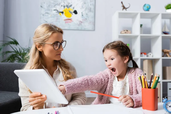 Маленька дитина кричить і вказує на цифровий планшет під час відвідування психолога — стокове фото
