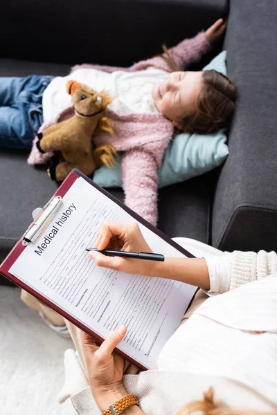Cropped view of psychologist writing in medical history while little girl telling problem — Stock Photo
