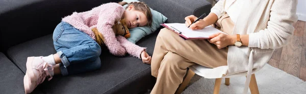 Little girl lying on sofa with toy while telling problem to psychologist, banner — Stock Photo