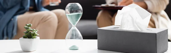 Horizontal banner of hourglass, plant and tissues on foreground — Stock Photo