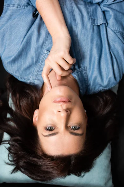 Top view of pensive brunette woman lying on pillow with finger on chin — стоковое фото