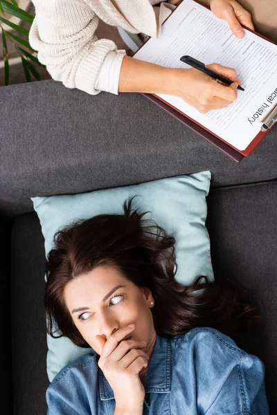 Terrified brunette woman covering mouth while therapist writing in medical history — Stock Photo