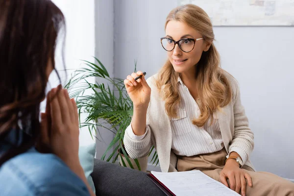 Femme blonde thérapeute pointant avec stylo sur le patient — Photo de stock