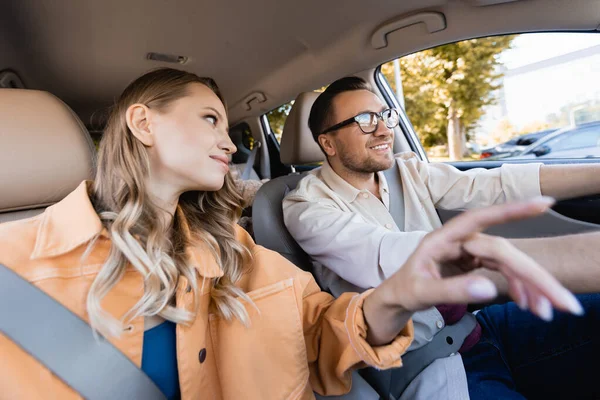 Smiling woman looking at husband while pointing with finger on blurred foreground in car — Stock Photo