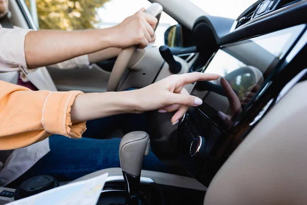 Vista recortada de la mujer que utiliza el sistema de audio en el coche, mientras que el marido conduce sobre fondo borroso - foto de stock