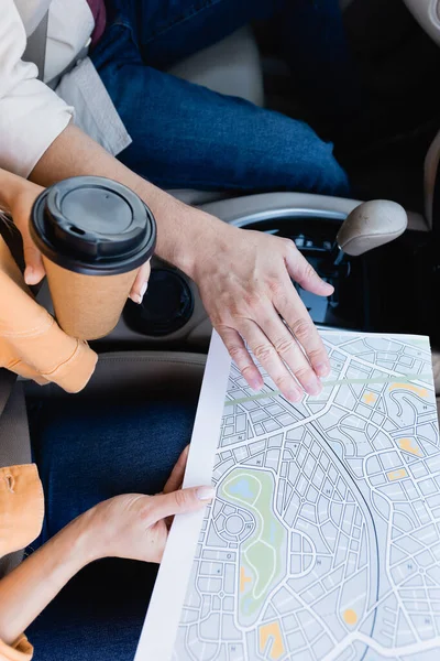 Ausgeschnittene Ansicht einer Frau, die Karte und Kaffee in der Hand hält, um ihrem Mann im Auto nahe zu kommen — Stockfoto