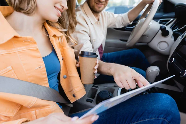 Cropped view of man pointing at map near smiling wife with coffee to go in car — Stock Photo