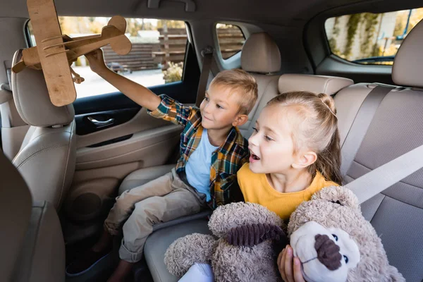 Bambini allegri con giocattoli seduti sul sedile posteriore di auto — Foto stock