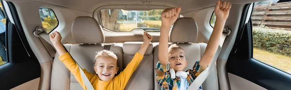 Cheerful children showing yeah gesture while sitting in auto, banner — Stock Photo