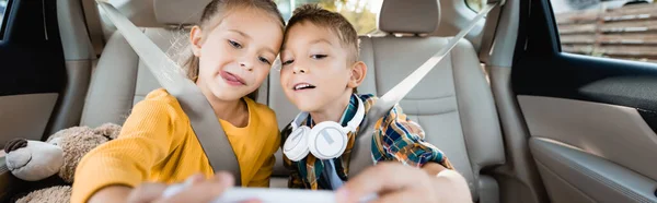 Enfants avec écouteurs et jouets prenant selfie sur smartphone en voiture, bannière — Photo de stock