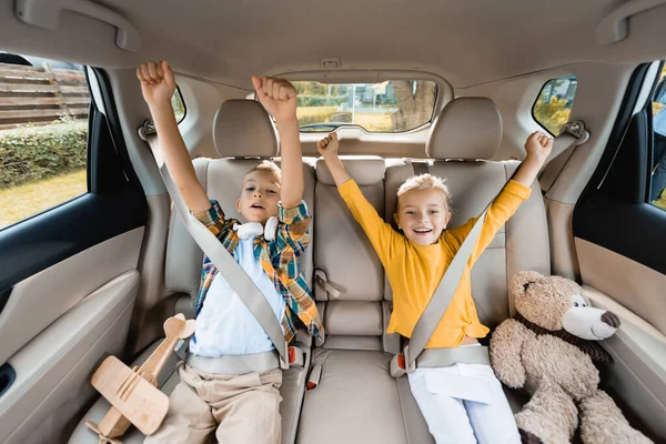 Lächelnde Kinder zeigen Ja-Geste, während sie neben Spielzeug im Auto sitzen — Stockfoto