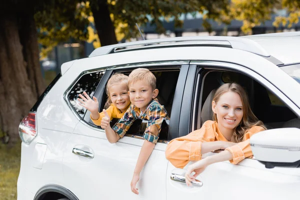 Lächelnde Kinder winken und zeigen sich im Urlaub wie eine nahe Mutter im Auto — Stockfoto