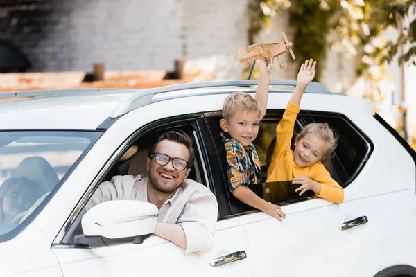 Smiling man looking at camera near wife and kids with toy in car — Stock Photo