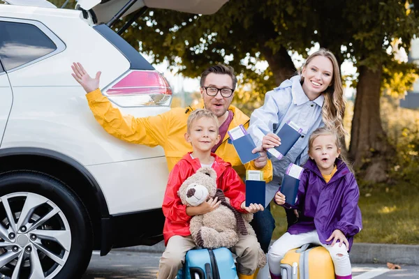 Cheerful family holding passports with air tickets near car outdoors — Stock Photo