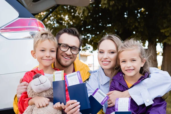 Cheerful family holding passports and air tickets near auto outdoors — Stock Photo
