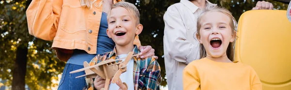 Niños alegres con avión de juguete de pie cerca de los padres con la maleta al aire libre, pancarta - foto de stock