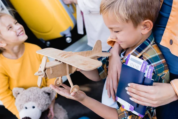 Sonriente niño sosteniendo avión de juguete cerca de la madre con pasaportes y billetes de avión sobre fondo borroso - foto de stock