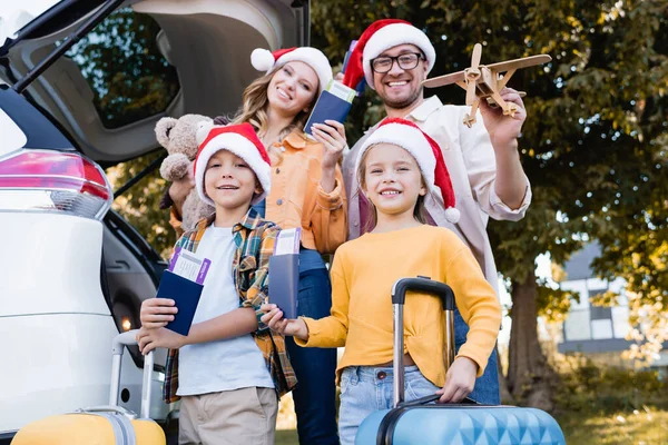 Family in santa hats holding passports with air tickets near suitcases and car outdoors — Stock Photo