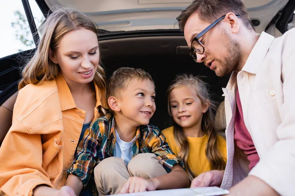 Cheerful family looking at map on blurred foreground near car trunk — Stock Photo