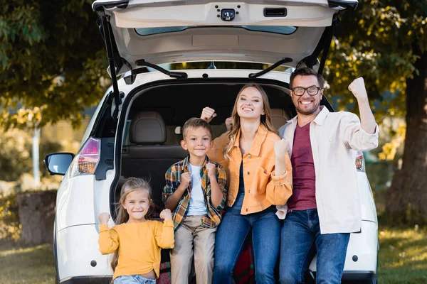 Веселая семья показывает да жест возле багажника автомобиля на открытом воздухе — стоковое фото