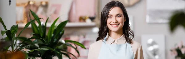 Glücklicher Blumenhändler lächelt in die Kamera im Blumenladen auf verschwommenem Hintergrund, Banner — Stockfoto