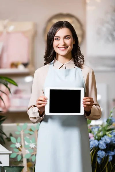 Lächelnder Blumenhändler, der in die Kamera schaut, während er ein digitales Tablet mit leerem Bildschirm auf verschwommenem Hintergrund hält — Stockfoto