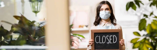 Florist in protective mask holding board with closed lettering on blurred foreground, banner — Stock Photo