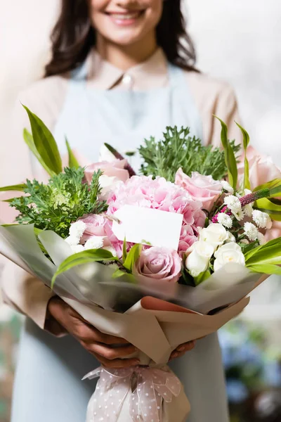 Cropped view of florist holding festive bouquet with empty tag on blurred background — Stock Photo