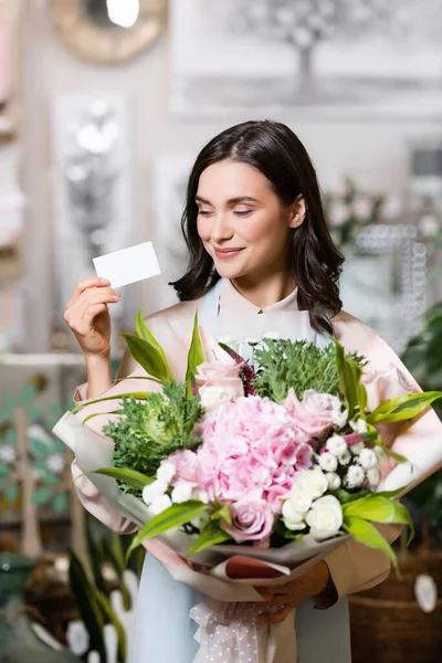 Fröhlicher Blumenhändler blickt auf leere Visitenkarte, während er festlichen Strauß im Blumenladen hält — Stockfoto