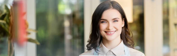 Fröhlicher Blumenhändler blickt in die Kamera in der Nähe von Blumenladen auf verschwommenem Hintergrund, Banner — Stockfoto